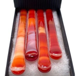 May include: Four glass stirring sticks in a box. The sticks are red, orange, and white with a marbled effect.
