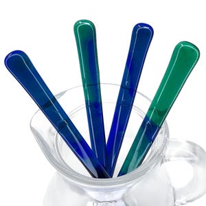 May include: Four glass stirring sticks in a clear glass jug. The sticks are blue and green with a marbled effect.