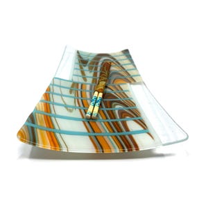 A rectangular glass tray with an upturned edge displays a marbled brown, orange, and white pattern crossed with turquoise stripes, holding chopsticks.