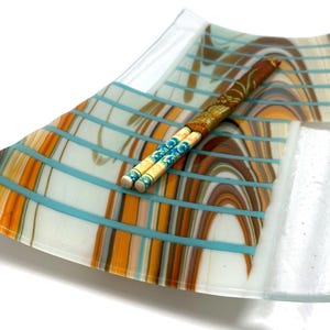 A rectangular curved glass tray with a Southwest pattern in brown, white, and turquoise stripes, holding a decorative chopstick set.