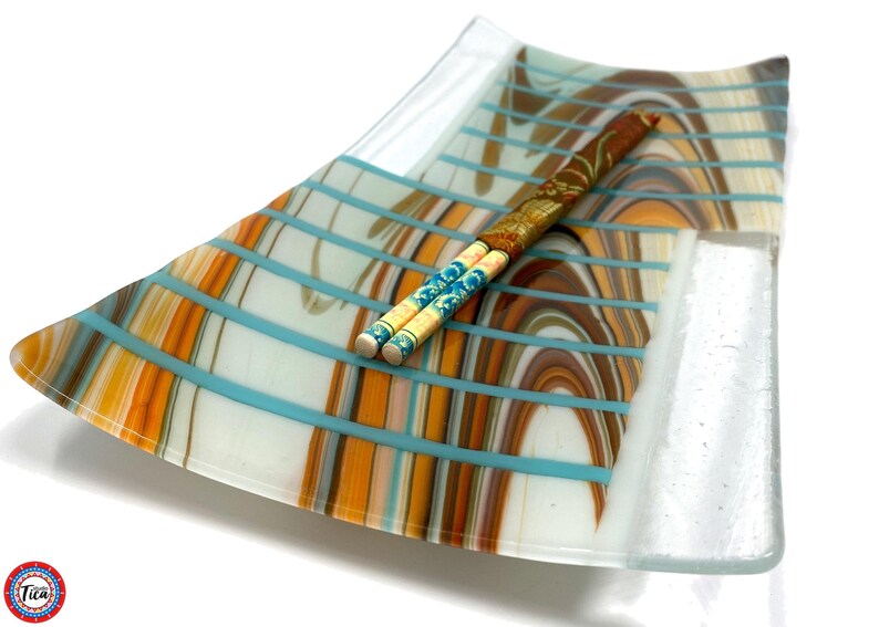 A rectangular curved glass tray with a Southwest pattern in brown, white, and turquoise stripes, holding a decorative chopstick set.