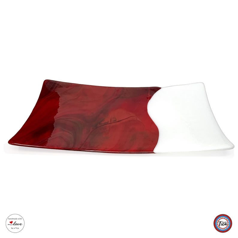 A curved glass tray lies horizontally on a white background, showing a large red marbled section on the left and a smaller white section on the right.