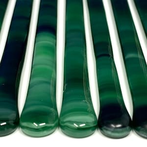 May include: A set of ten green glass mosaic tiles with a swirled pattern. The tiles are approximately 6 inches long and have rounded ends.