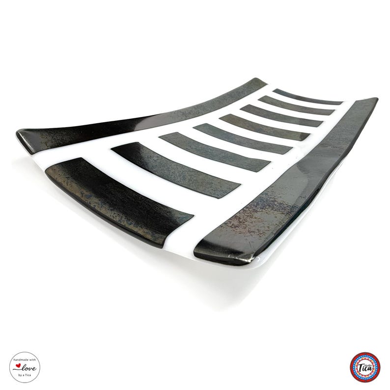 An angled view of a rectangular curved glass tray with a white base and dark, textured vertical stripes.