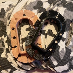 Peut inclure: Un assortiment de patchs de tissu circulaires avec un motif de camouflage noir, blanc et gris. Deux cadres en forme de U, l'un rose clair et l'autre noir, sont placés sur les patchs.