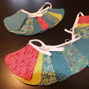 May include: A handmade fabric banner with alternating teal, green, yellow, and red fabric triangles. The banner has white ribbon ties and features a variety of patterns including floral, polka dot, and geometric designs.