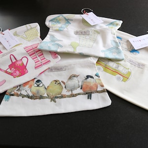 May include: Five fabric hanging storage bags with different patterns. The bags are white with colorful designs. One bag has a pattern of pink rain boots, a pink watering can, and green watering cans. Another bag has a pattern of blue birds and birdhouses. Another bag has a pattern of colorful birds on a branch. Another bag has a pattern of yellow and blue cars. The last bag has a pattern of blue and green cars.