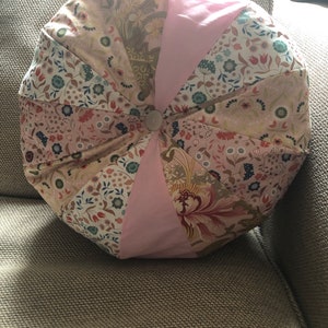 Könnte beinhalten: Ein rundes, rosa und floral gemustertes Kissen mit einem Knopf in der Mitte.