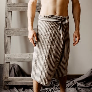 May include: A person wearing a striped linen wrap skirt. The skirt is tied at the waist and has a loose fit. The person is standing on a gray fabric surface.