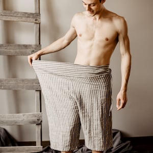 May include: A person wearing striped linen pants. The pants are loose fitting and have a wide waistband. The person is standing in front of a wooden ladder.