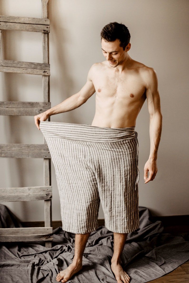 May include: A person wearing striped linen pants. The pants are loose fitting and have a wide waistband. The person is standing in front of a wooden ladder.