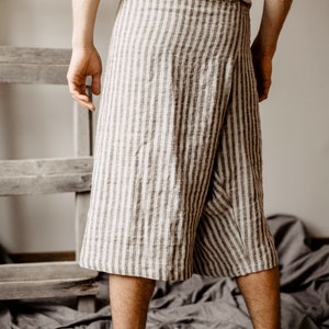 May include: A person wearing a striped linen wrap skirt. The skirt is tied at the waist and has a relaxed fit. The person is standing on a gray fabric surface.