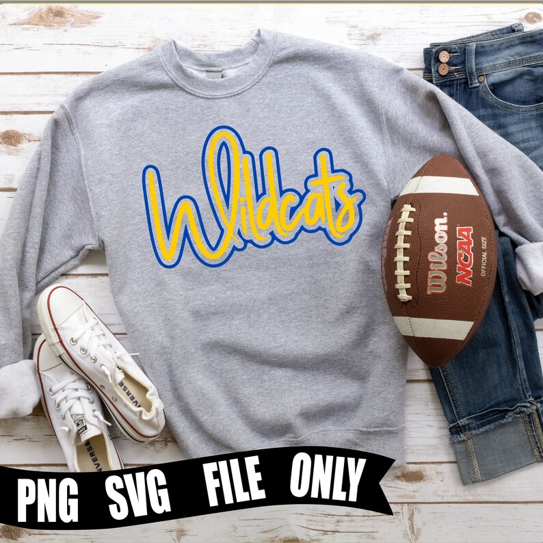 May include: Gray sweatshirt with the word "Wildcats" in yellow and blue lettering. The sweatshirt is laying on a white wooden surface with a football and jeans.