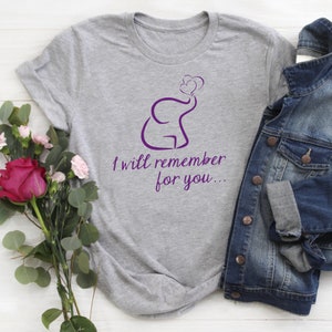 Puede incluir: Una camiseta gris con un diseño de elefante morado que sopla corazones. El texto "Te recordaré..." está impreso debajo del elefante.
