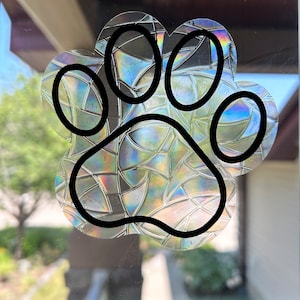 Peut inclure: Un autocollant de patte de chien noir avec un motif iridescent en vitrail. L'autocollant est appliqué sur une porte en verre.