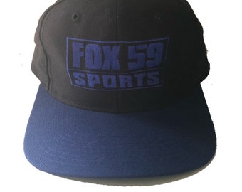 May include: A black and blue baseball cap with the embroidered text "FOX 59 SPORTS" in blue.