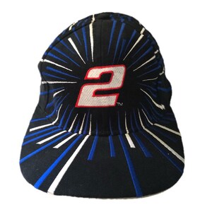 May include: A black baseball cap with a white and blue starburst pattern. The number "2" is in the center of the cap in white with a red outline. The text "TM" is below the number.