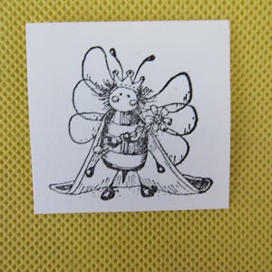 May include: A black and white illustration of a bee queen wearing a crown and holding a flower. The bee has large wings and is wearing a cape. The image is on a white square.