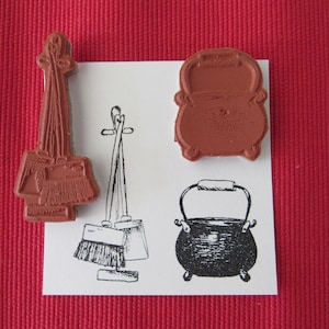 May include: Three rubber stamps with illustrations of a cauldron, a broom, and a set of brooms. The stamps are brown and are on a white background.