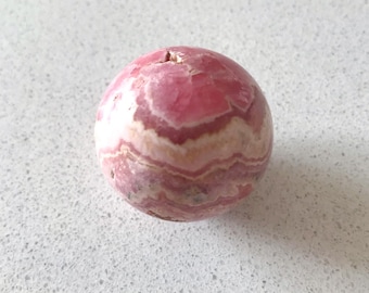 May include: A pink and white striped sphere of polished pink calcite, a type of mineral.