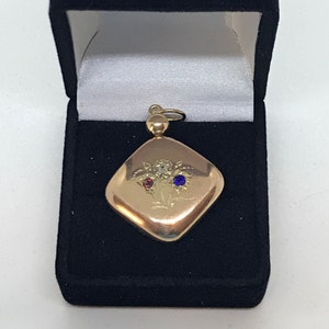 May include: A gold locket pendant with a diamond and red and blue gemstones set in a floral design. The locket is in a black velvet box.