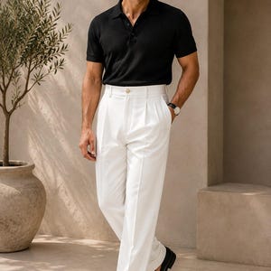 May include: A black short-sleeved polo shirt with a buttoned placket paired with high-waisted white trousers featuring front pleats and a single button closure. The outfit is completed with black leather loafers and a wristwatch on the left wrist.