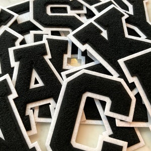 May include: A pile of black felt letters with white outlines. The letters are in a variety of sizes and are arranged in a random order. The letters are all uppercase and include the letters A, C, S, W, and T.