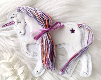 May include: White felt unicorn applique with a purple and orange yarn mane and tail. The unicorn has a purple star on its back and a pink ribbon tied around its mane.