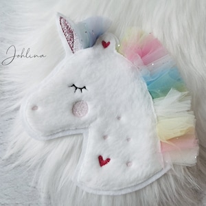 Könnte beinhalten: Weißer Plüsch-Einhornkopf mit einer Regenbogen-Tüllmähne und einem rosafarbenen Glitzerhorn. Das Einhorn hat gestickte Augen, eine rosa Nase und zwei rote Herzen.