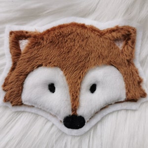 Könnte beinhalten: Ein braunes Plüsch-Fuchs-Kopf-Applik mit weißem Fell um die Augen und die Nase. Der Fuchs hat eine schwarze Nase und schwarze Augen.