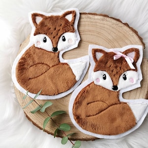 Könnte beinhalten: Zwei braune Plüsch-Fuchs-Applikationen mit weißen Filz-Akzenten. Ein Fuchs hat eine rosa Schleife auf dem Kopf.