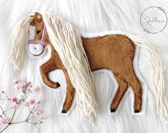 May include: A handmade felt horse toy with a brown body, white mane and tail, and a pink bridle. The horse is set against a white, fluffy background. The toy is designed with a whimsical, child-friendly aesthetic.
