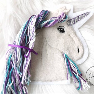 Könnte beinhalten: Weißer Einhorn-Applikationen mit einer Mähne und einem Schwanz aus lila, türkis, weiß und silberfarbenem Garn. Das Einhorn hat ein silbernes Glitzerhorn und schwarze gestickte Augen.