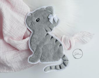 May include: A plush gray cat applique with dark gray stripes, a white stitched border, and a small white satin bow attached to the ear. The cat is depicted in a seated position with a long, striped tail curving along the bottom edge.