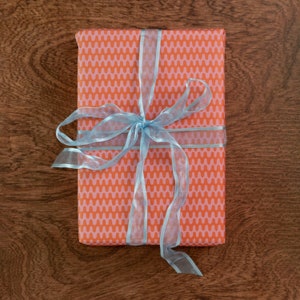 May include: A gift box wrapped in orange and pink patterned paper with a light blue ribbon tied in a bow.