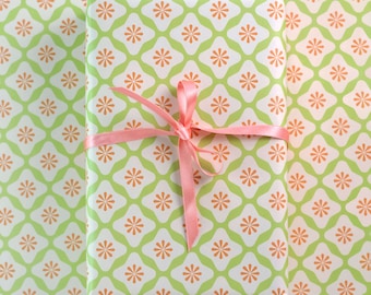 May include: A green and orange patterned gift wrap with a pink ribbon tied in a bow.