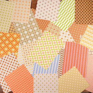 May include: A selection of patterned paper sheets in various colours and designs. The patterns include floral, geometric, and striped motifs in shades of orange, green, yellow, and brown. The papers are arranged on a wooden surface.