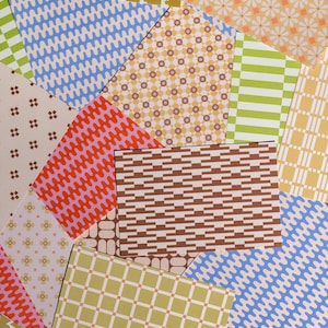 May include: A collection of rectangular paper sheets featuring various patterns including blue wavy lines, green and white stripes, brown geometric blocks, yellow plaid, orange floral prints, and small brown cross shapes on a cream background.