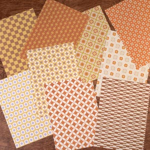 Könnte beinhalten: Eine Sammlung von Papieren mit verschiedenen Mustern und Farben. Die Muster umfassen Karos, Blumenmuster, geometrische Formen und Punkte. Die Farbpalette besteht aus Braun-, Orange-, Gelb- und Cremetönen, wodurch eine Retro-Ästhetik entsteht.