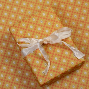 May include: A yellow gift box with a white and orange chequered pattern and a white satin ribbon. The box is wrapped in matching wrapping paper.