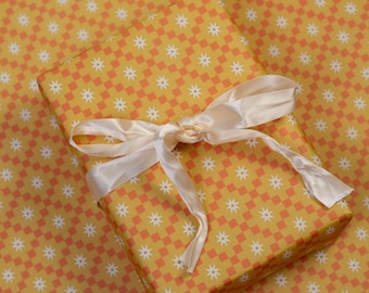 May include: A yellow gift box with a white and orange checkered pattern and a white satin ribbon. The box is wrapped in matching wrapping paper.