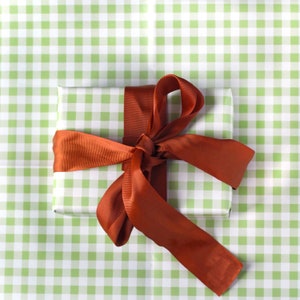 May include: A white gift box with a green and white gingham pattern is wrapped with a large orange satin bow.