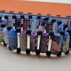 May include: A bracelet made of rolled up paper with different text and designs. The paper is rolled into small cylinders and strung together with black beads.