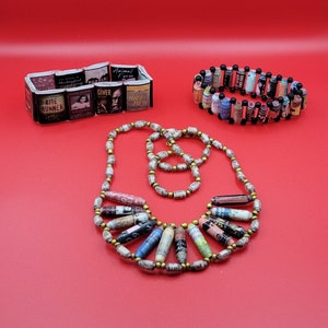 May include: A necklace and bracelet made of rolled paper beads. The beads are decorated with book covers, including titles like "Kite Runner", "Animal Farm", and "The Giver".
