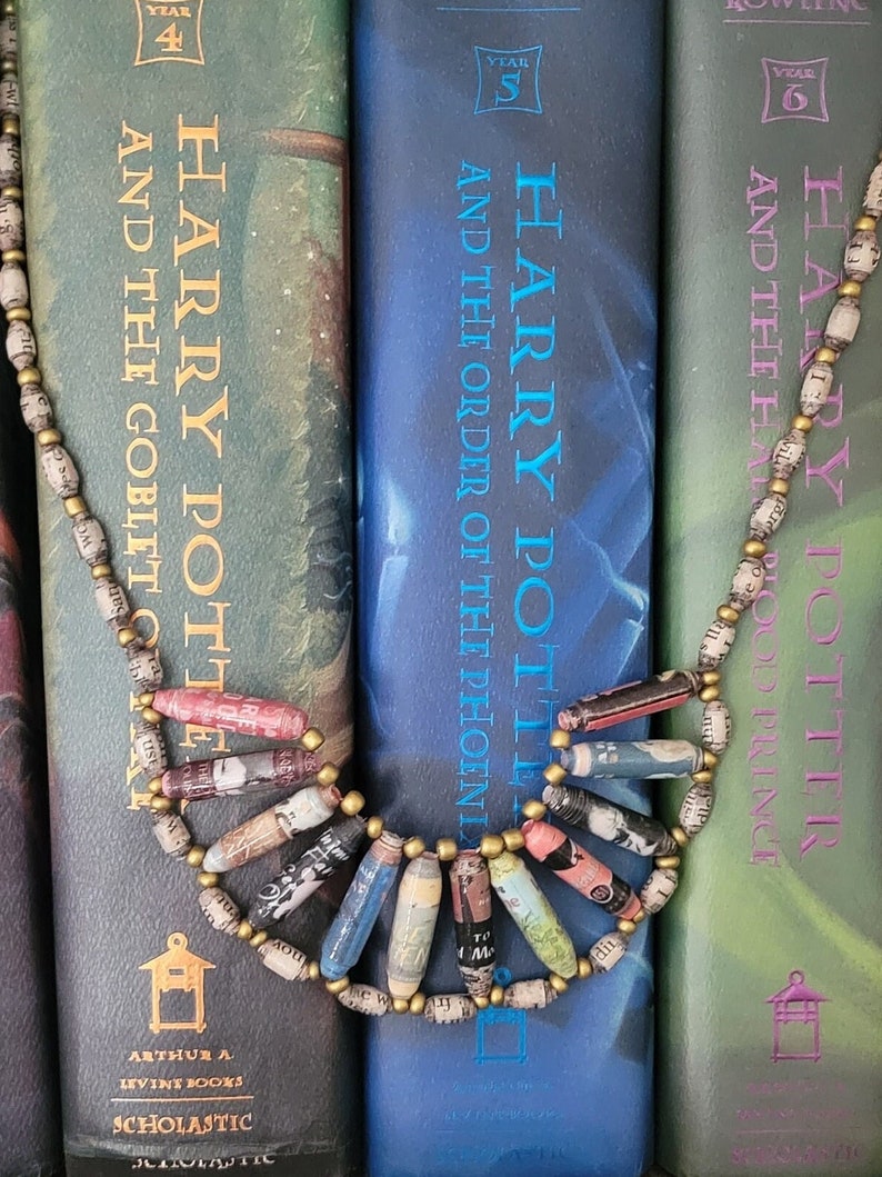 May include: Three Harry Potter books, volumes 4, 5, and 6, with a paper bead necklace in front of them. The books are green, blue, and green, and the necklace is made of brown and white paper beads.