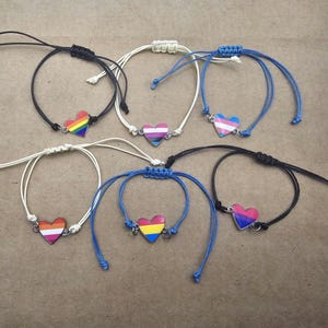 May include: Six bracelets with different colored heart charms. The charms are rainbow, transgender, bisexual, lesbian, pansexual, and genderfluid.