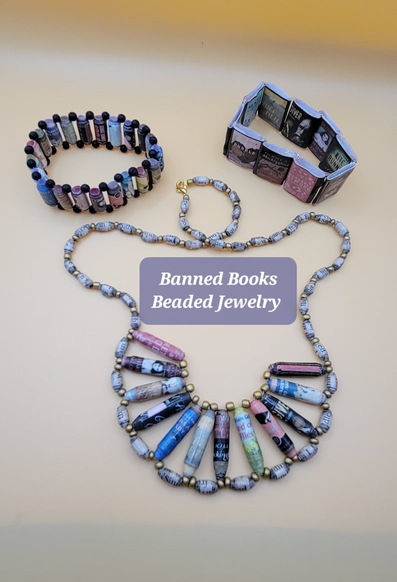 May include: A set of three necklaces made from rolled up pages of banned books. The necklaces are in different lengths and styles. The necklaces are made with gold and black beads. The necklaces are labeled "Banned Books Beaded Jewelry".