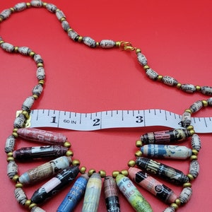 May include: A necklace made of paper beads with gold accents. The beads are rolled from pages of books and magazines, and some have visible text. The necklace is 18 inches long and has a clasp closure.