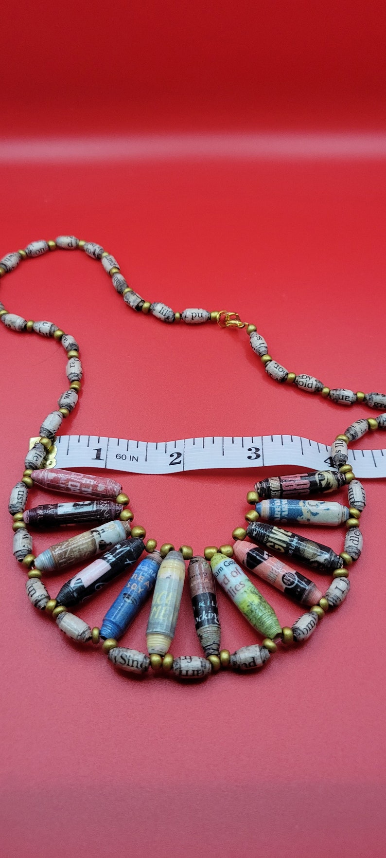 May include: A necklace made of paper beads with gold accents. The beads are rolled from pages of books and magazines, and some have visible text. The necklace is 18 inches long and has a clasp closure.