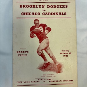 May include: A vintage 1941 Brooklyn Dodgers vs. Chicago Cardinals football program from Ebbets Field. The off-white cover features red text and a central illustration of a football player in uniform with the number 9, identified as Perry Schwartz.